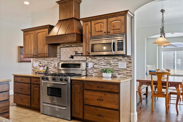 kitchen with light stone counters, stainless steel appliances, custom range hood, and tasteful backsplash