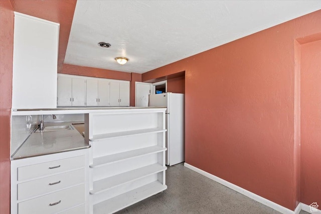 kitchen with stainless steel counters, baseboards, speckled floor, white cabinetry, and freestanding refrigerator