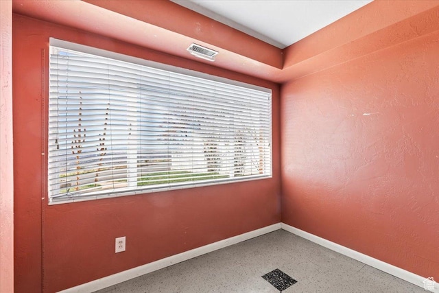 empty room featuring baseboards, visible vents, and speckled floor
