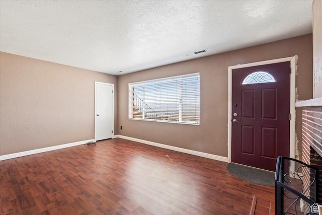 foyer entrance featuring visible vents, a textured ceiling, baseboards, and wood finished floors