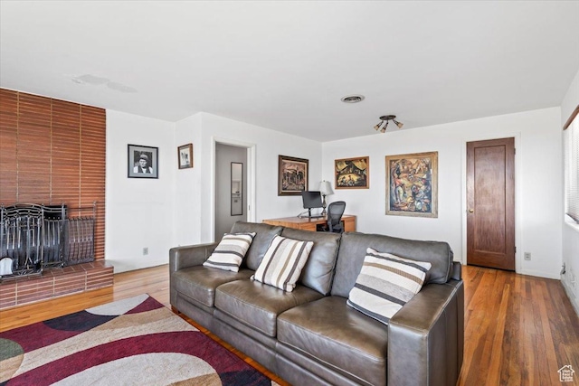 living room featuring wood finished floors, a brick fireplace, and visible vents
