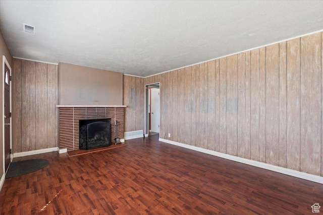 unfurnished living room featuring a tiled fireplace, wood finished floors, wood walls, baseboards, and visible vents
