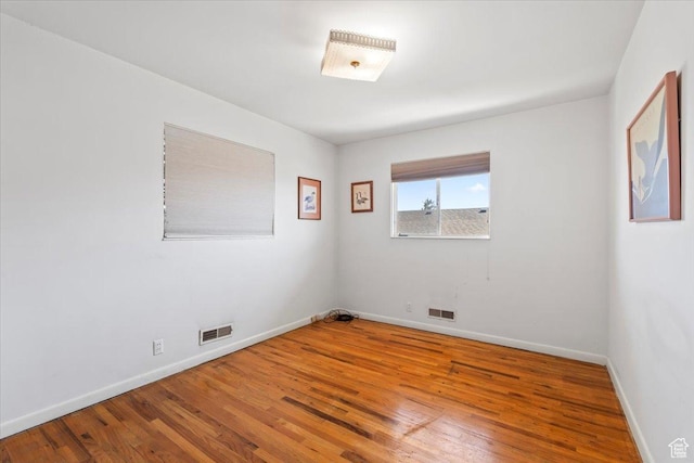 unfurnished room with baseboards, visible vents, and hardwood / wood-style flooring