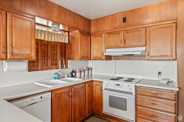 kitchen with light countertops, a sink, brown cabinetry, under cabinet range hood, and white appliances