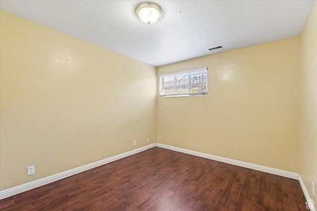 empty room featuring wood finished floors, baseboards, and visible vents