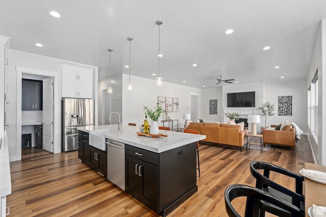 kitchen featuring a sink, appliances with stainless steel finishes, a center island with sink, white cabinets, and ceiling fan