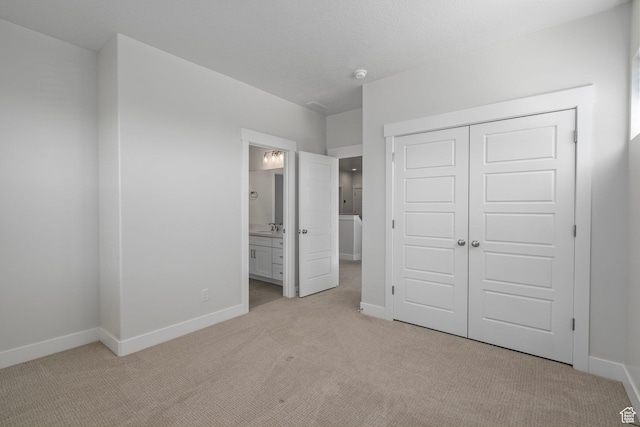 unfurnished bedroom featuring a closet, connected bathroom, baseboards, and light colored carpet