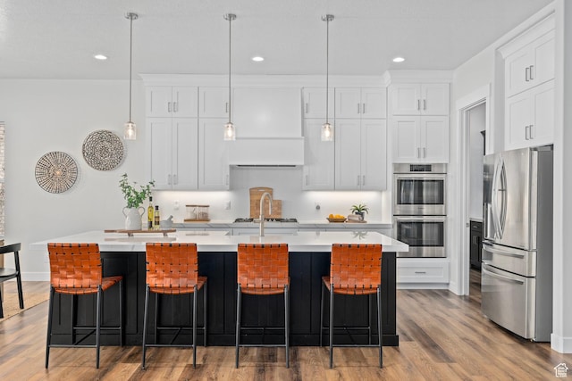 kitchen featuring light countertops, an island with sink, white cabinets, appliances with stainless steel finishes, and wood finished floors