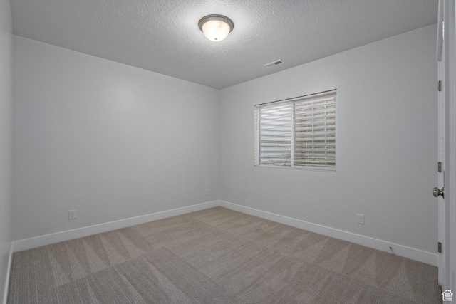 spare room featuring light carpet, a textured ceiling, baseboards, and visible vents