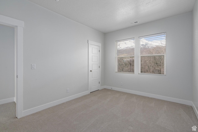 unfurnished room featuring light colored carpet, visible vents, baseboards, and a textured ceiling