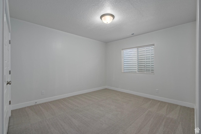 empty room with a textured ceiling, baseboards, light colored carpet, and visible vents