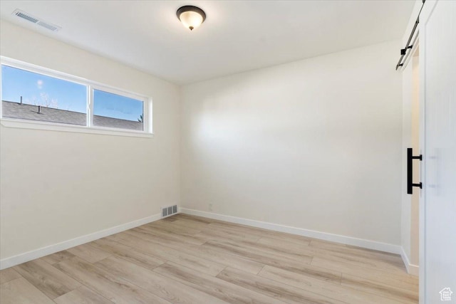 unfurnished room featuring baseboards, a barn door, visible vents, and light wood finished floors