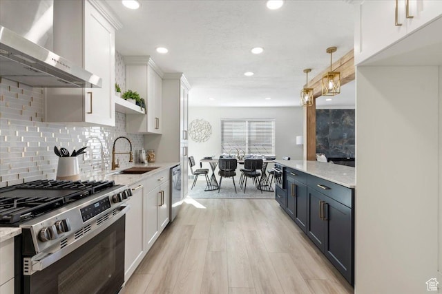 kitchen featuring a sink, white cabinetry, appliances with stainless steel finishes, light wood-type flooring, and wall chimney range hood