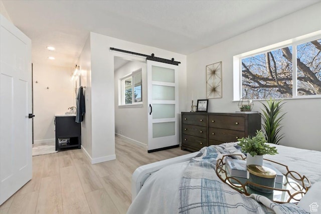 bedroom featuring multiple windows, light wood-type flooring, a barn door, and baseboards