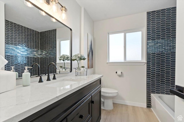 full bathroom featuring toilet, vanity, wood finished floors, a bathtub, and baseboards