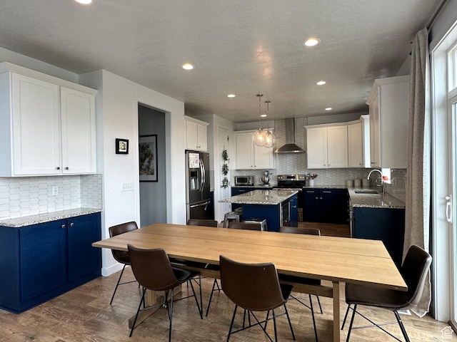 2685 E White Birch Dr, Eagle Mountain, UT 84005 - kitchen featuring stainless steel appliances, wall chimney range hood, blue cabinets, a sink, and a kitchen island