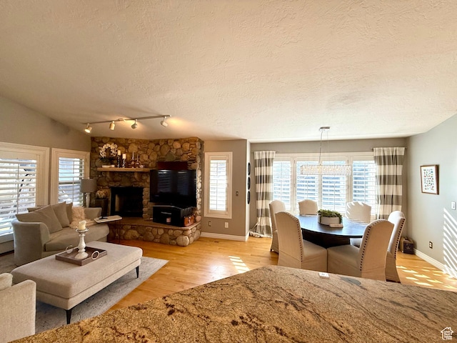 6991 S Canyon Pines Cir E, Cottonwood Heights, UT 84121 - living area with a textured ceiling, a stone fireplace, light wood-style flooring, rail lighting, and baseboards