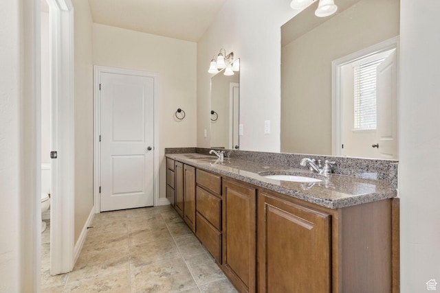 full bathroom with double vanity, a sink, toilet, and baseboards