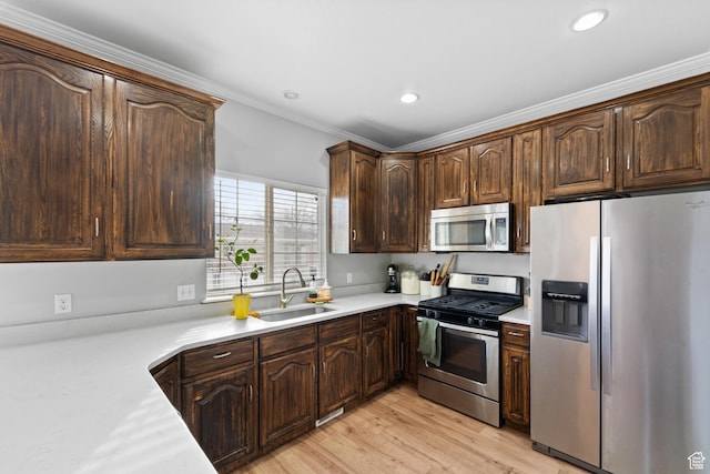 kitchen featuring light countertops, stainless steel appliances, dark brown cabinetry, a sink, and light wood-type flooring