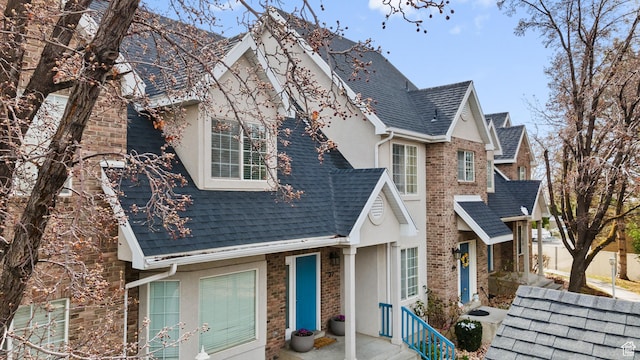 view of front facade with stone siding, stucco siding, and a shingled roof