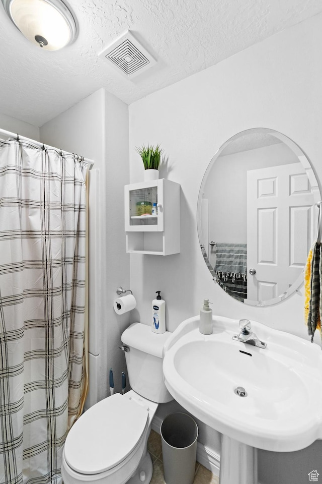 bathroom featuring a shower with shower curtain, toilet, a sink, a textured ceiling, and visible vents