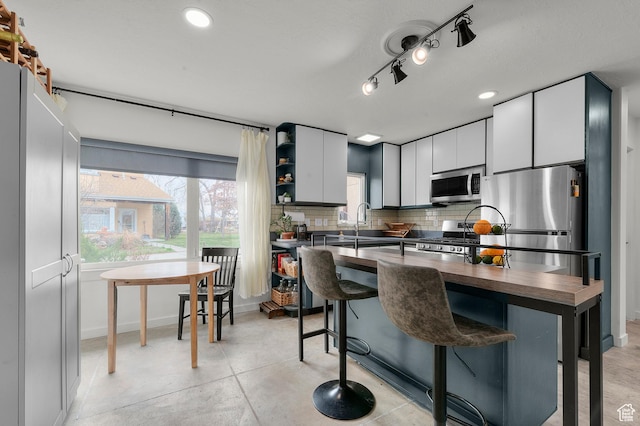 kitchen with a kitchen breakfast bar, white cabinetry, tasteful backsplash, baseboards, and appliances with stainless steel finishes