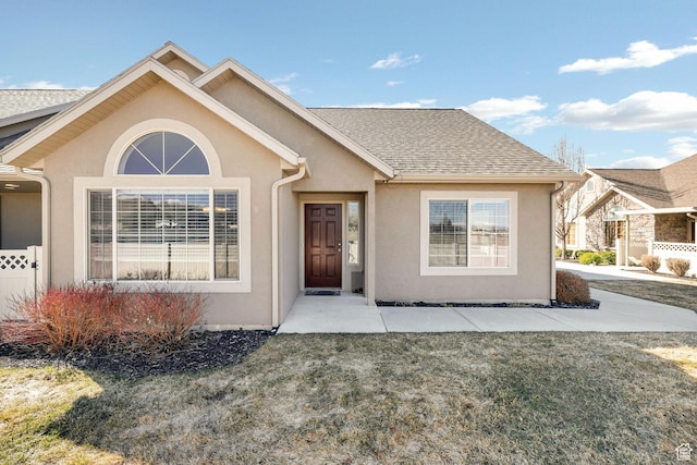 ranch-style home featuring a front yard, stucco siding, and roof with shingles