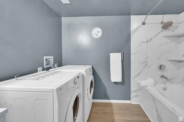 laundry room with laundry area, a textured ceiling, light wood finished floors, baseboards, and washing machine and dryer