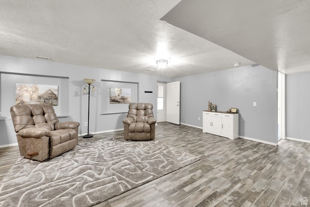 living area featuring visible vents, a textured ceiling, baseboards, and wood finished floors
