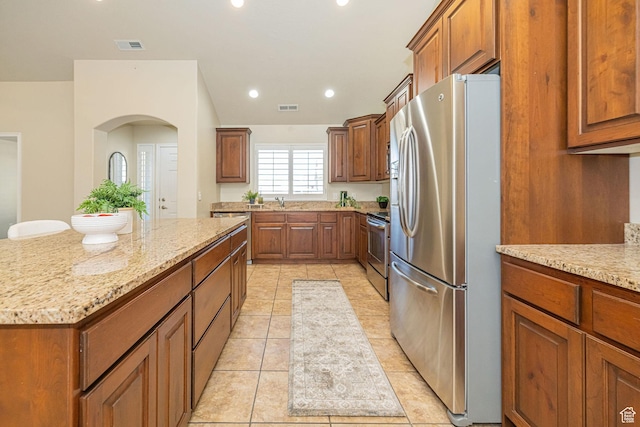 1886 S 830 W Unit D, Syracuse, UT 84075 - kitchen with light stone counters, appliances with stainless steel finishes, a center island, brown cabinetry, and visible vents