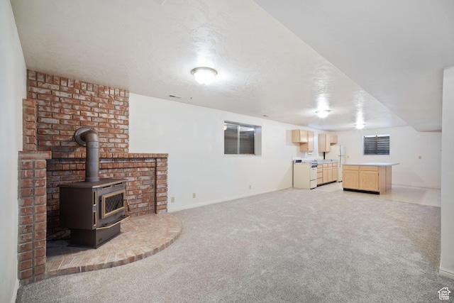 unfurnished living room featuring baseboards, a textured ceiling, a wood stove, and light carpet