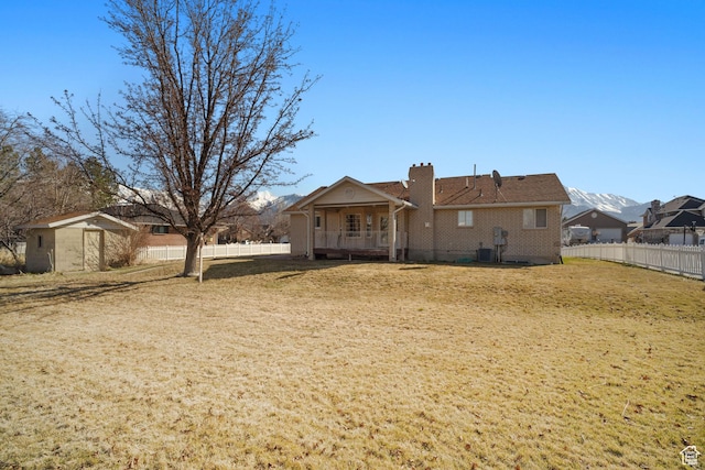 back of house featuring central air condition unit, fence, a chimney, a mountain view, and a yard