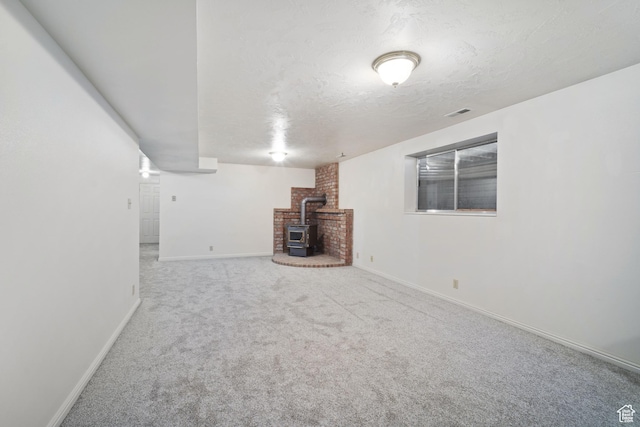 finished basement featuring baseboards, a wood stove, carpet, and a textured ceiling