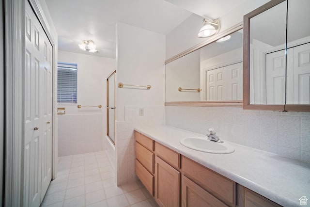 full bath with tile patterned floors, vanity, wainscoting, enclosed tub / shower combo, and tile walls