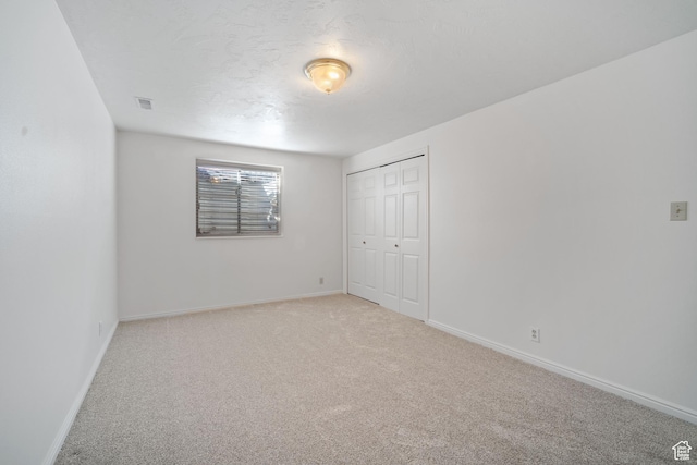 unfurnished bedroom featuring a closet, light carpet, a textured ceiling, baseboards, and visible vents