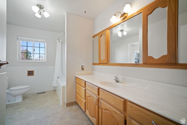 bathroom featuring a wainscoted wall, toilet, vanity, visible vents, and tile walls