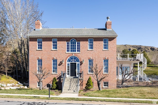 view of front of property with a chimney, a shingled roof, brick siding, and a front yard