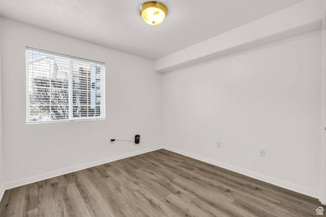 unfurnished room with baseboards, wood finished floors, and a textured ceiling