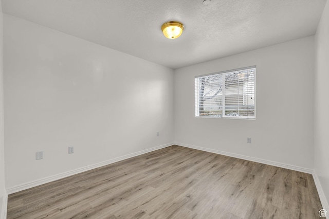 spare room featuring a textured ceiling, baseboards, and wood finished floors