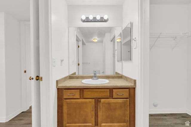 bathroom featuring vanity, a walk in closet, baseboards, and wood finished floors