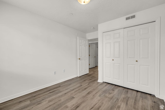 unfurnished bedroom featuring a closet, a textured ceiling, visible vents, baseboards, and wood finished floors