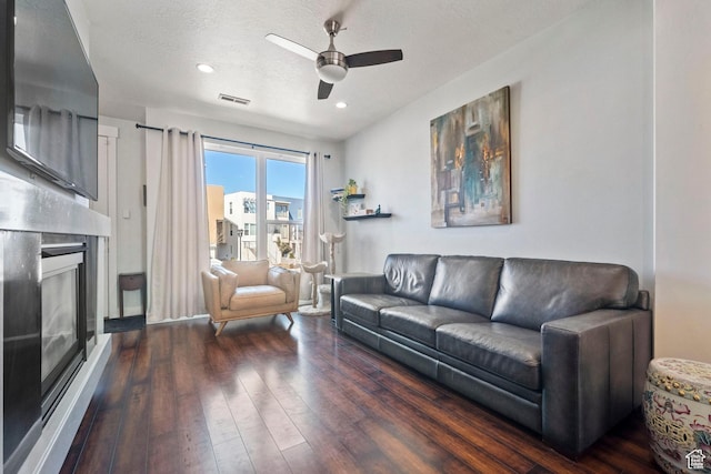 living area with a textured ceiling, visible vents, a ceiling fan, a fireplace, and wood finished floors