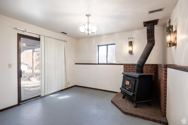 unfurnished living room featuring a wood stove, an inviting chandelier, concrete floors, baseboards, and visible vents