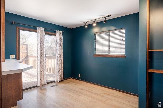 empty room featuring baseboards, visible vents, wood finished floors, and track lighting