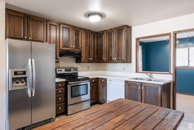 kitchen featuring light countertops, stainless steel appliances, dark brown cabinetry, under cabinet range hood, and a sink