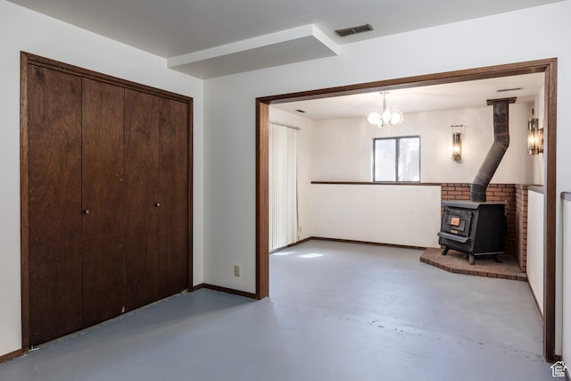 interior space featuring a wood stove, concrete floors, baseboards, visible vents, and a notable chandelier