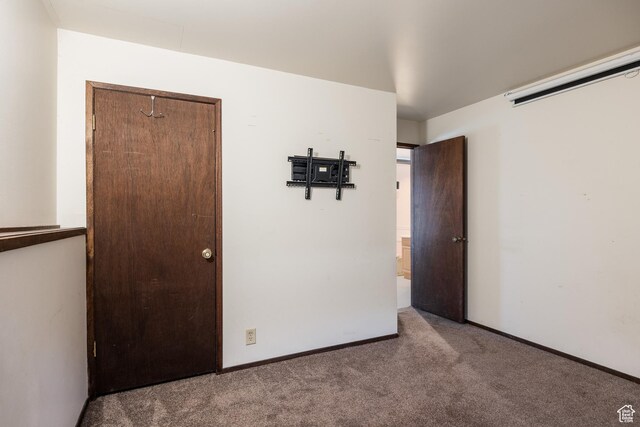 unfurnished bedroom with baseboards, a wall mounted AC, and carpet