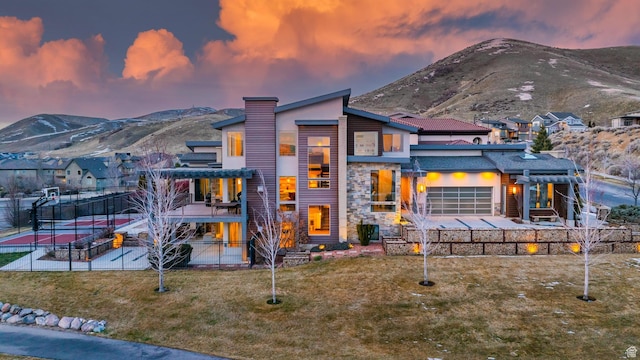4601 N Toscana Hills Dr, Lehi, UT 84043 - back of property at dusk featuring fence, an attached garage, a mountain view, a yard, and a chimney