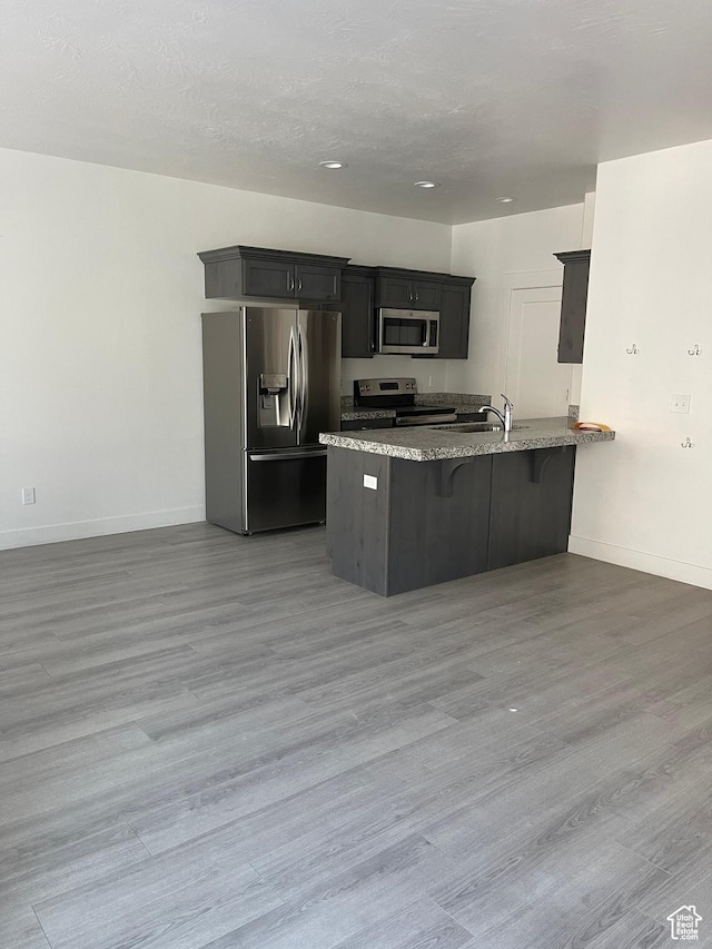 4937 E Lake Dr, Eagle Mountain, UT 84005 - kitchen featuring a peninsula, baseboards, light stone countertops, appliances with stainless steel finishes, and a kitchen breakfast bar