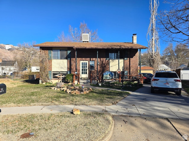 raised ranch featuring brick siding, a chimney, concrete driveway, and a front yard